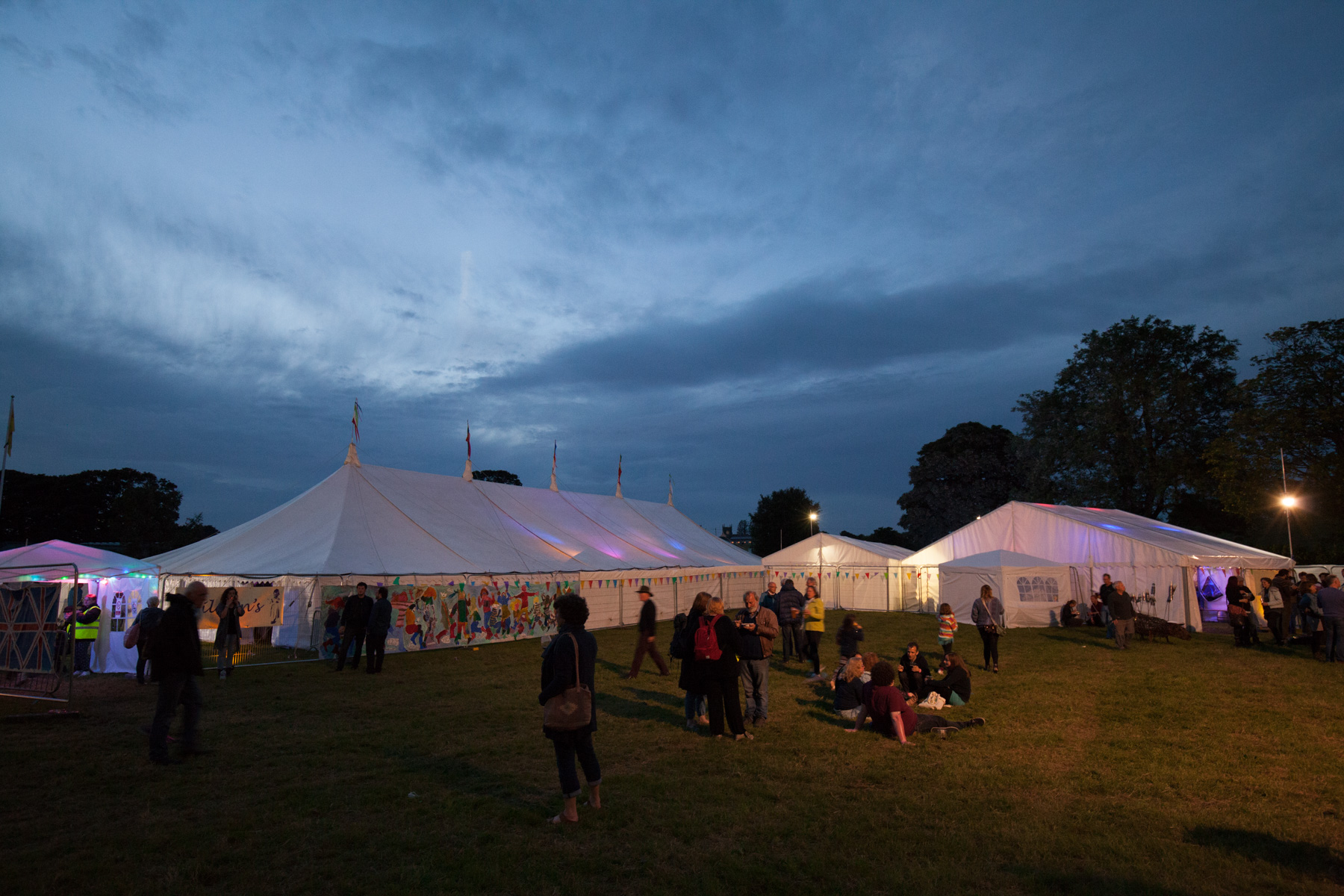 The Priddy Folk Festival site at dusk with people sitting on the grass.